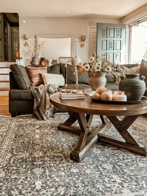 a welcoming earthy living room with a grey sofa and earhty pillows a printed rug a stained round table and some candles